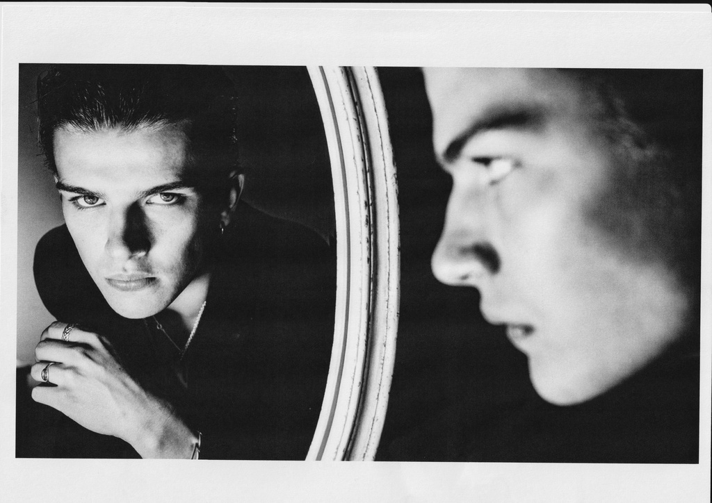 Black and white portrait of a man looking into a round mirror, showing his reflection and profile.