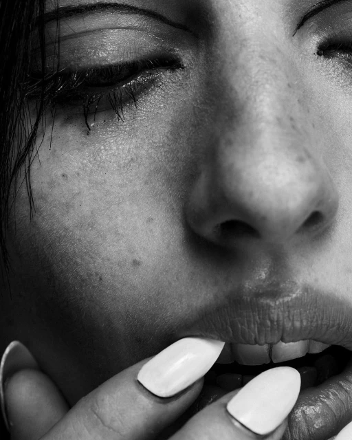 Close-up black and white portrait of a woman's face with a hand with long white nails near her mouth, showcasing beauty and detail.