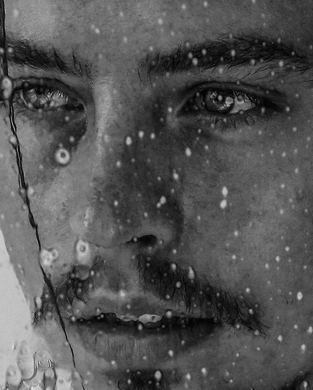 Monochrome portrait of a man's face with water droplets, creating an intimate and textured visual, enhancing the face's details.