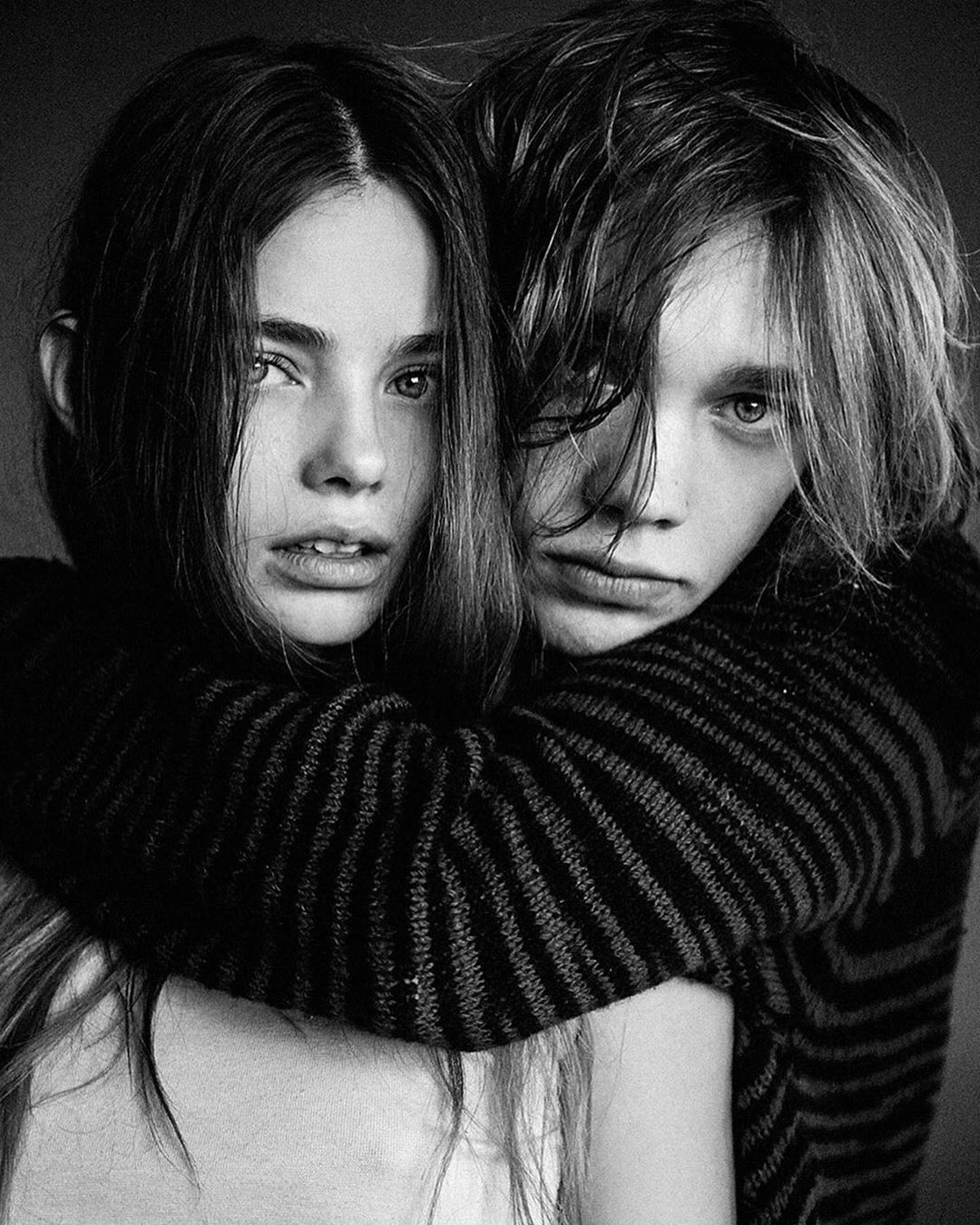 Black and white portrait of a woman and man embracing while wearing striped sweaters. The couple is indoors in a photo studio.