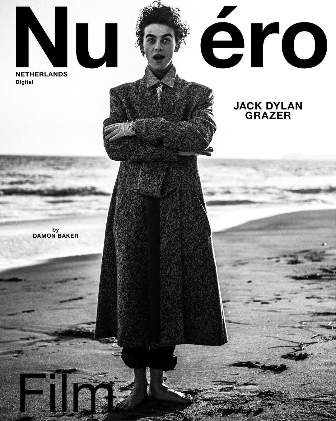 Black-and-white fashion magazine cover featuring Jack Dylan Grazer in a patterned overcoat on a sandy beach, minimalist design.