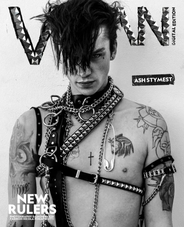 Monochrome portrait of Ash Stymest on a magazine cover, wearing leather harness and chains. The background is off-white, and the image features tattoos.
