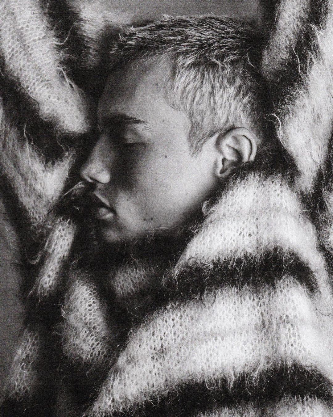 Close-up monochrome profile portrait of a young man wrapped in a thick, textured striped knit scarf by Damon Baker.