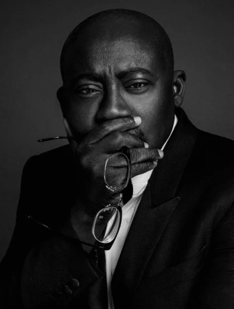 Monochrome portrait of a Black man wearing a dark blazer, holding glasses near his face by Damon Baker