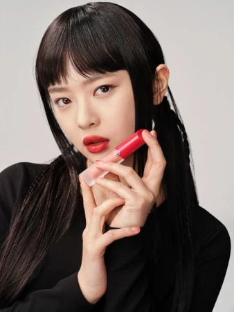 Asian woman with red lipstick holds a tube of lipstick in a close-up shot on a light background for a beauty advertisement.