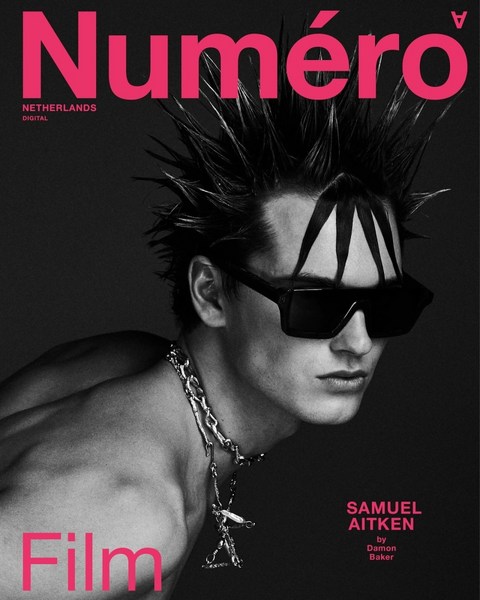 Black and white portrait of a model on a magazine cover with a spiky hairstyle, dark sunglasses, and a thick silver chain necklace.