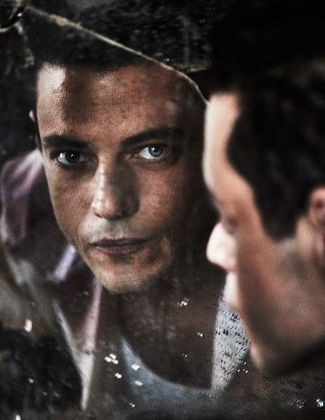 Portrait of a reflective man looking into a broken mirror, his visage split and doubled in the shattered glass of a photo studio.