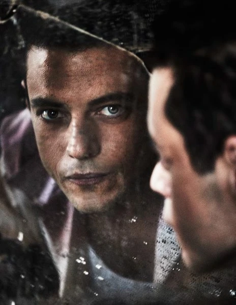 Portrait of a reflective man looking into a broken mirror, his visage split and doubled in the shattered glass of a photo studio.