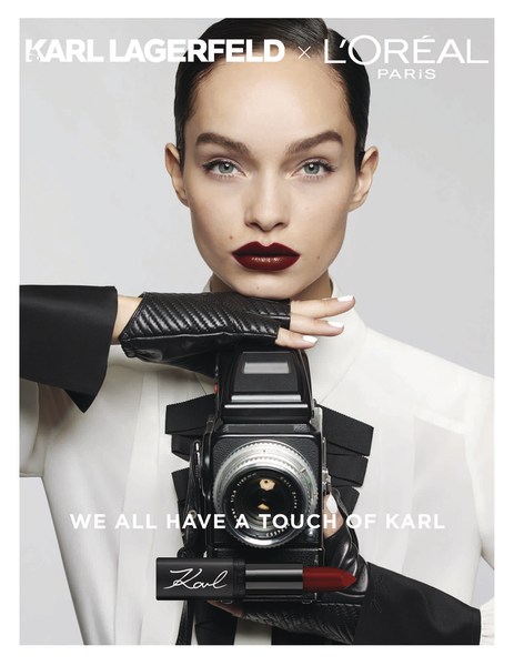 Glamorous beauty ad featuring a woman holding a camera and lipstick with Karl Lagerfeld and L'Oréal Paris branding against a white background.