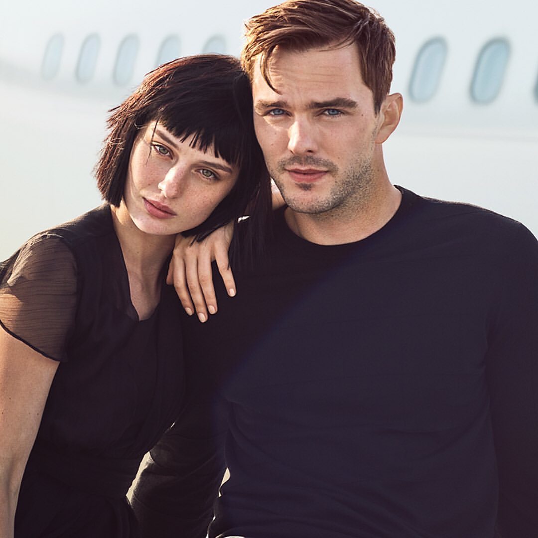 Portrait of a man and a woman in black clothing posed against the exterior of an airplane fuselage.