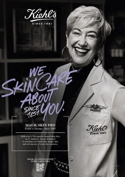 Smiling woman in lab coat, Kiehl's brand ad featuring skincare products and text overlays. Shot in a photo studio with a black and white color palette.