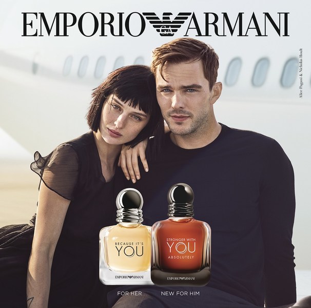 Emporio Armani fragrance ad featuring a man and woman posing in front of a plane, with bottles of cologne in the foreground.