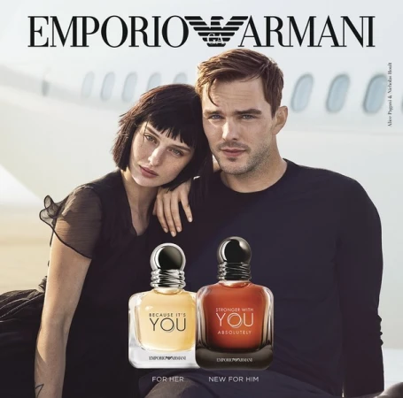 Emporio Armani fragrance ad featuring a man and woman posing in front of a plane, with bottles of cologne in the foreground.