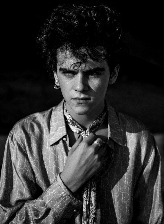 Monochrome portrait of a young man with dark curly hair wearing a patterned silk shirt and necktie by photographer Damon Baker