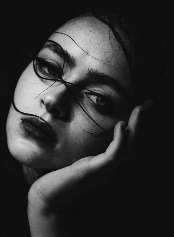 Close up monochrome portrait of a young woman resting her chin in her hand with dark strands of hair curving across her face