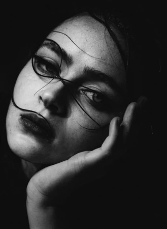 Close up monochrome portrait of a young woman resting her chin in her hand with dark strands of hair curving across her face