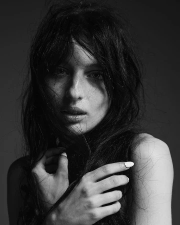Close-up portrait of a woman with long dark messy hair and light eyes photographed by Damon Baker.