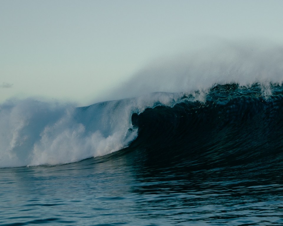 Large wave breaking in the ocean with white foamy spray in a wide shot, showcasing the power and beauty of nature.
