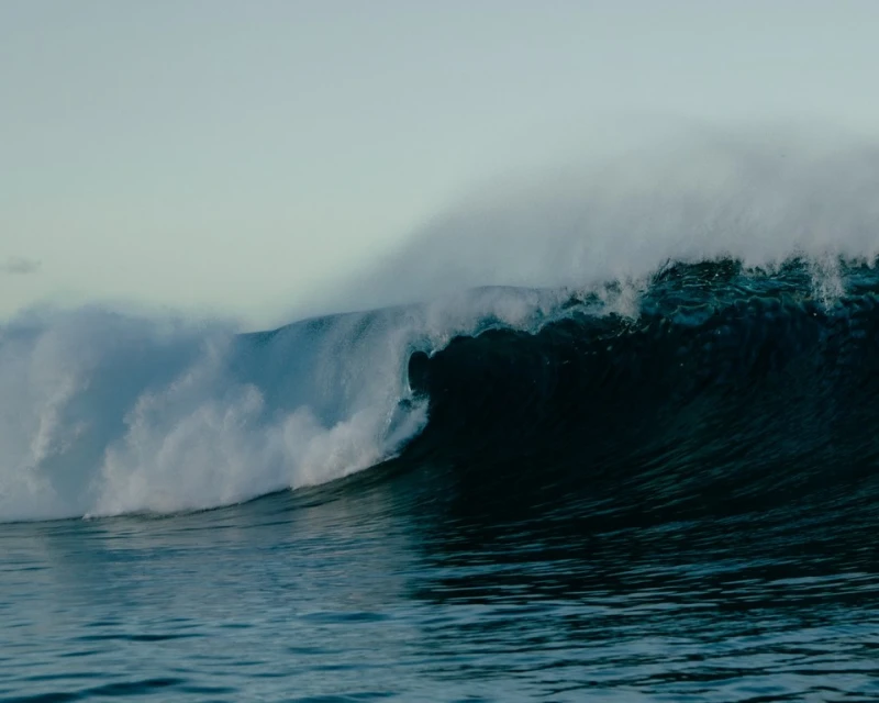 Large wave breaking in the ocean with white foamy spray in a wide shot, showcasing the power and beauty of nature.
