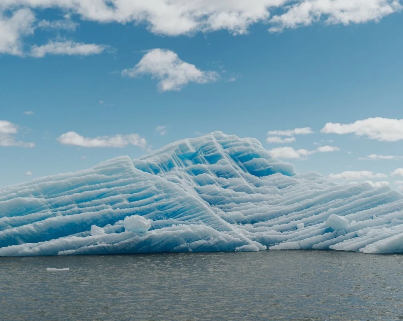 Striking view of a blue-striped glacier floating in calm water under a partly cloudy sky, creating a serene Arctic landscape.