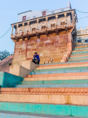 Man seated on large outdoor stone steps next to a dog beneath an ornate building with columns.