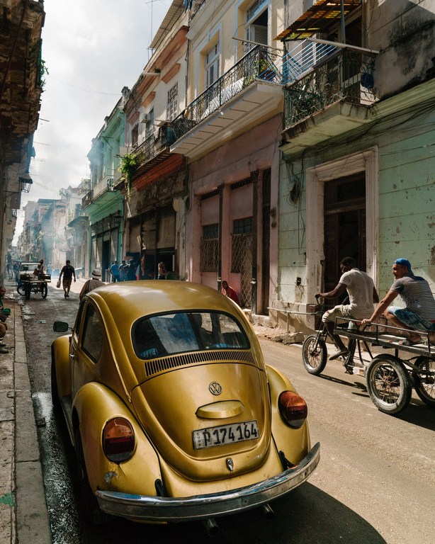 Vintage golden yellow Volkswagen Beetle parked on a street in Havana, Cuba, with colorful colonial buildings in the background.