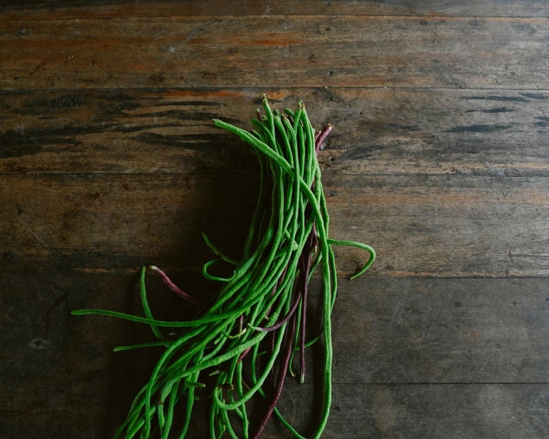 Overhead shot of a bunch of yardlong beans with green and purple pods, arranged on a rustic dark brown wooden plank surface.