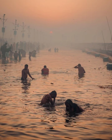 People bathing and wading in a misty river at sunrise, captured in a wide atmospheric shot by Dan Tom.