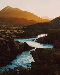 Aerial view of a winding blue river flowing through steep mountainous terrain at sunset by Dan Tom