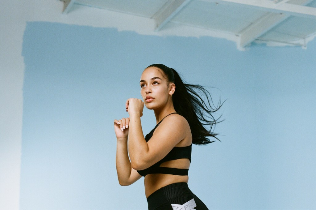 Athletic woman in workout clothes poses against a light blue background in a fitness setting, looking up and to the side.