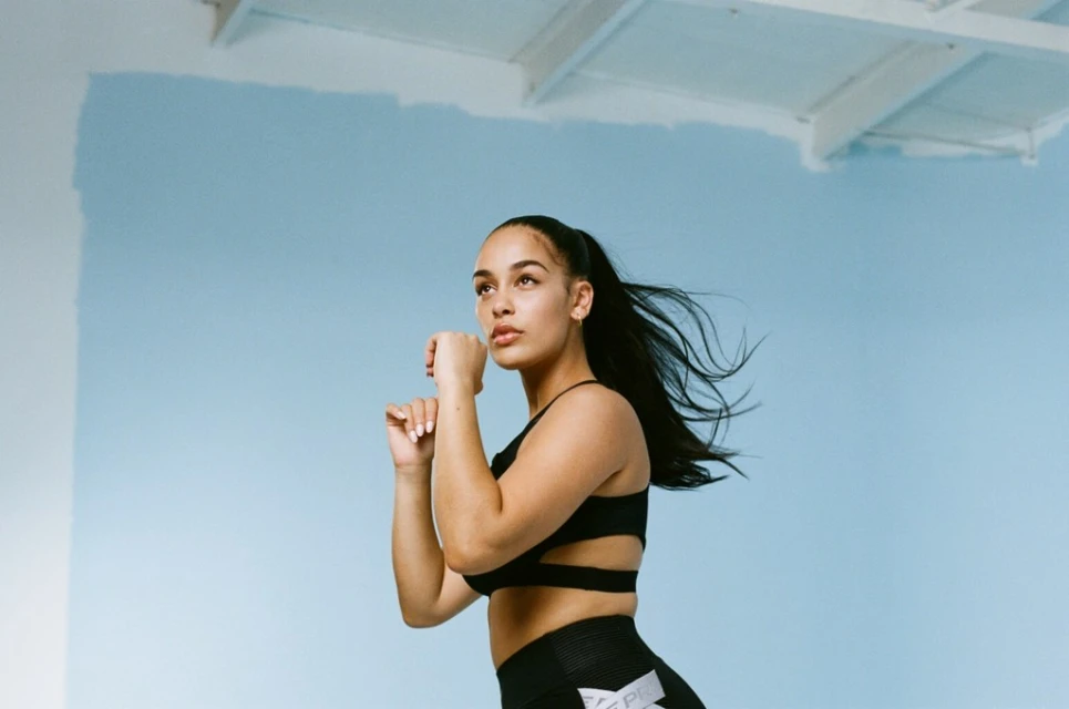 Athletic woman in workout clothes poses against a light blue background in a fitness setting, looking up and to the side.