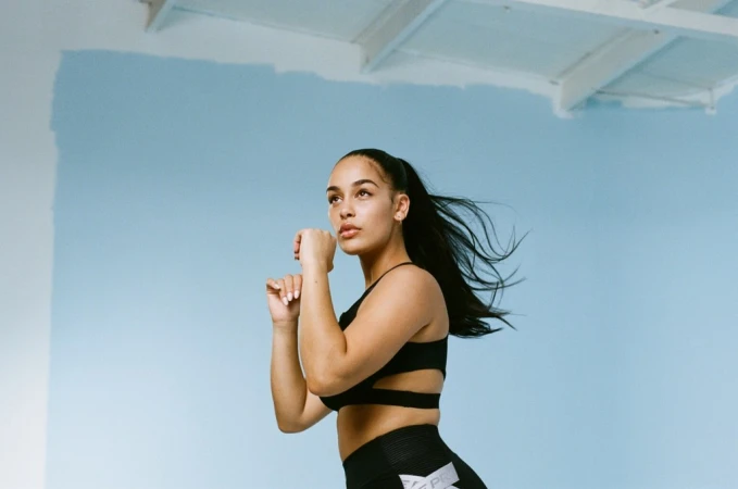Athletic woman in workout clothes poses against a light blue background in a fitness setting, looking up and to the side.