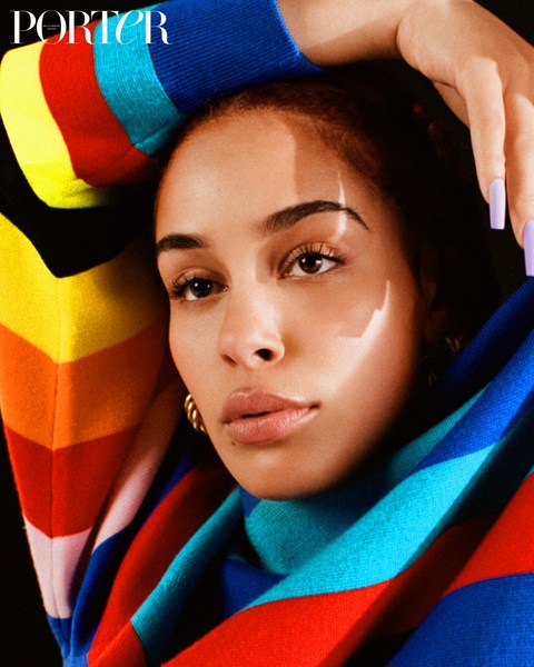 Close-up of a woman with light skin, light eyes, and short hair, wearing a striped top, with manicured nails, and gold hoop earrings.