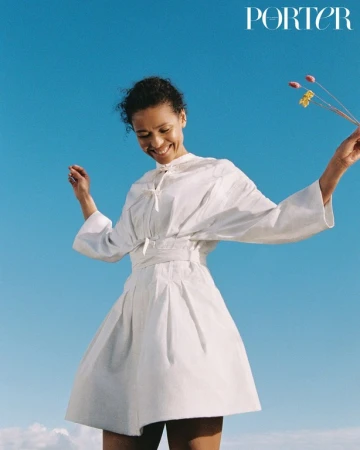 Smiling woman in white dress holding wildflowers against a clear blue sky, photographed by Danika Magdelena.