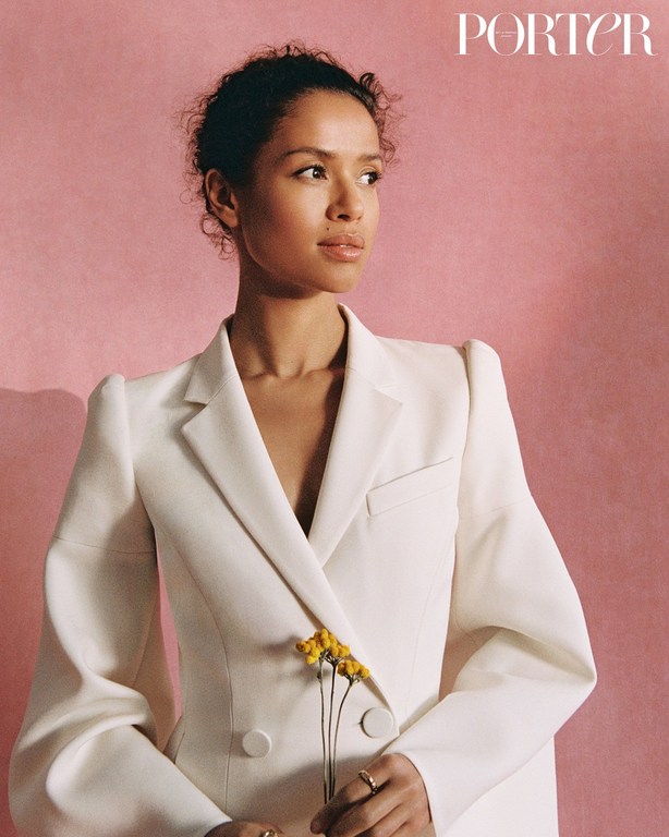 Gugu Mbatha-Raw wearing a white blazer holding yellow flowers against a pink background by Danika Magdelena