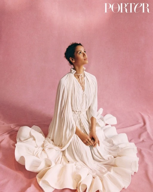 Woman in elegant white dress sitting on pink fabric looking up, studio shot, fashion editorial, Porter magazine cover, beauty.