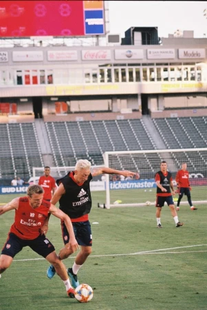 Two soccer players compete for the ball on a grass field in front of a stadium, illuminated by stadium lights during a soccer match.