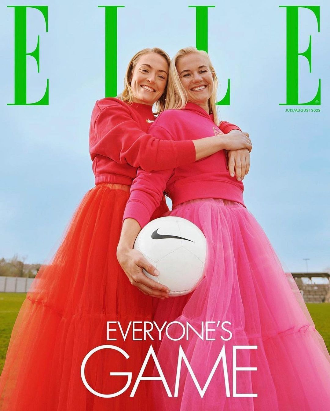 Two women, Elle magazine cover, sport fashion concept. Athletes embrace outdoors wearing tulle skirts, holding soccer ball, sunny sky.
