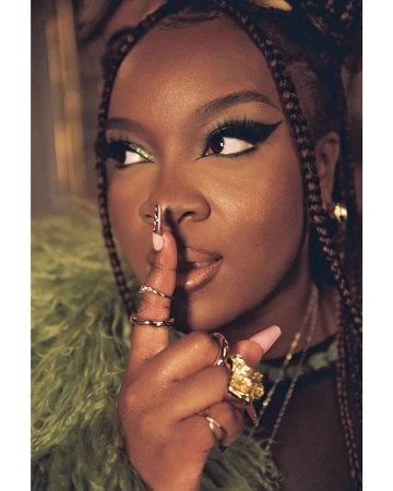 Close-up portrait of a Black woman holding a finger to her lips with bold winged eyeliner and green eyeshadow, styled by Danika Magdelena