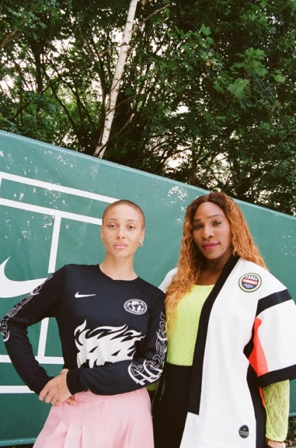 Two female athletes, one with a shaved head and the other with long hair, pose against a backdrop featuring a tennis court graphic.
