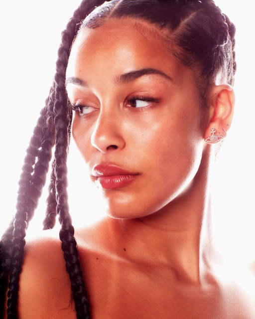 Close-up portrait of a black woman with braided hair, showcasing glossy lips, bare shoulders, and jewelry against a bright, diffused background.