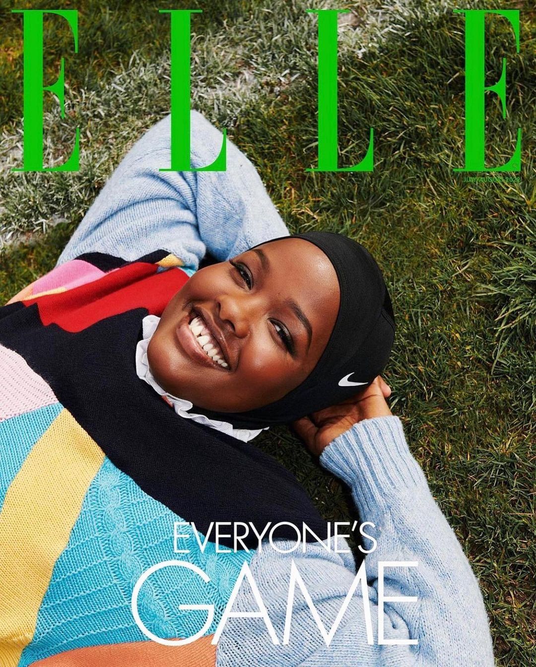 Magazine cover featuring a smiling Black woman in a colorful sweater and Nike headscarf, lying on grass with the bright green ELLE masthead.