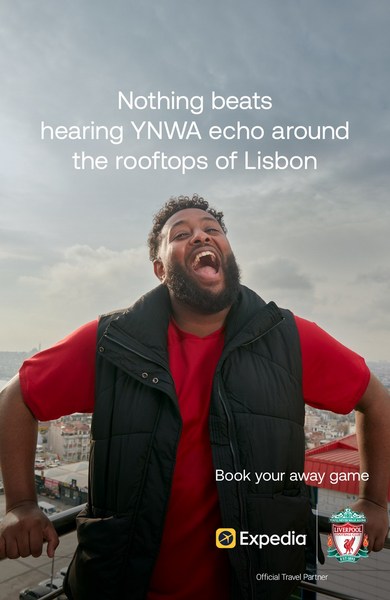 Enthusiastic man in vest smiles on Lisbon rooftop promoting travel with Expedia and Liverpool Football Club logo on travel ad.