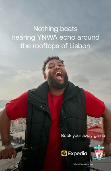 Enthusiastic man in vest smiles on Lisbon rooftop promoting travel with Expedia and Liverpool Football Club logo on travel ad.
