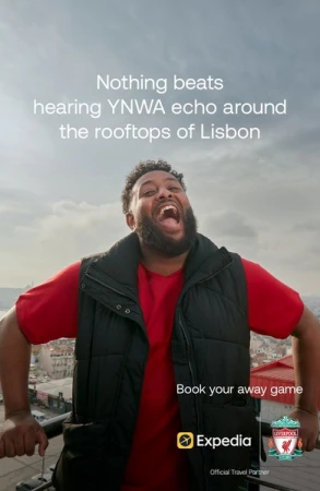 Enthusiastic man in vest smiles on Lisbon rooftop promoting travel with Expedia and Liverpool Football Club logo on travel ad.