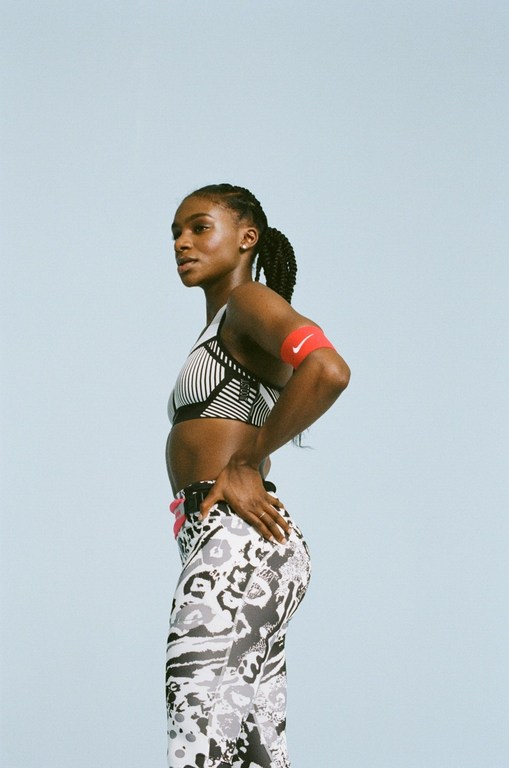 Athletic woman in fitness wear poses in a medium shot against a plain blue background, showcasing sport style and healthy lifestyle.