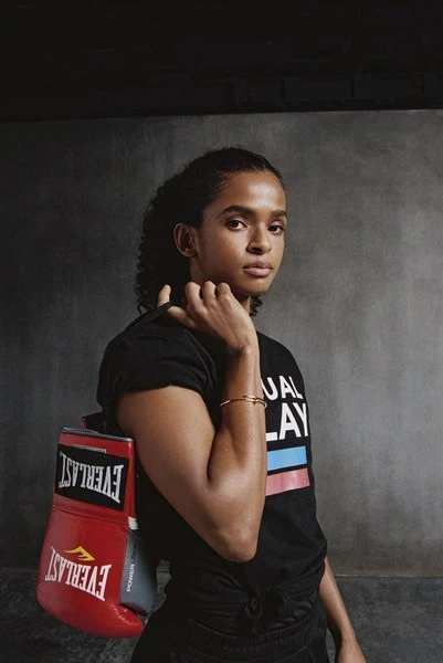 Athletic woman in a t-shirt poses with red Everlast boxing gloves indoors with a neutral expression in a medium shot, indoor setting.