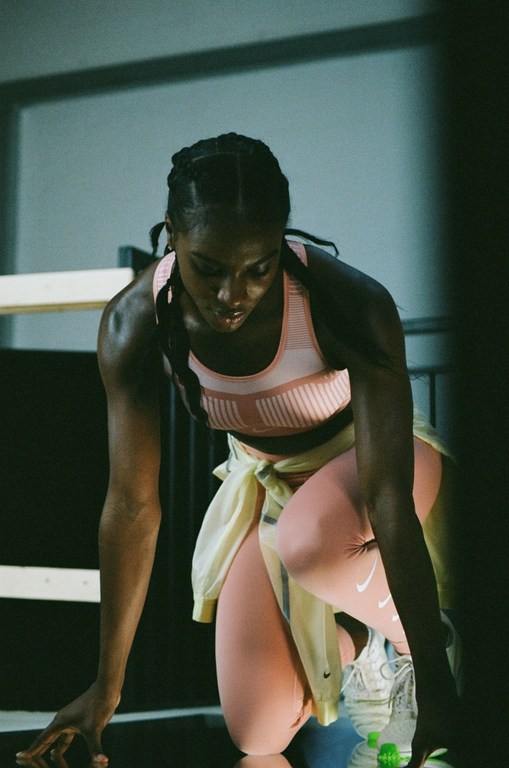 Focused female athlete in sportswear kneeling, poised for action. Fitness photoshoot in indoor athletic setting with determination.