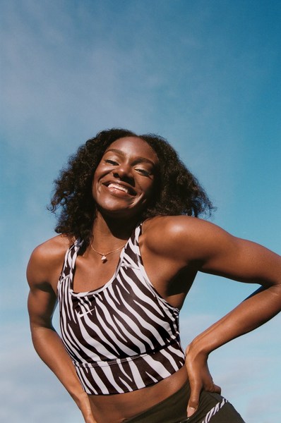 Smiling black woman wearing a zebra print sports crop top against a clear blue sky background
