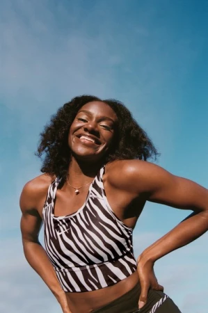 Smiling black woman wearing a zebra print sports crop top against a clear blue sky background